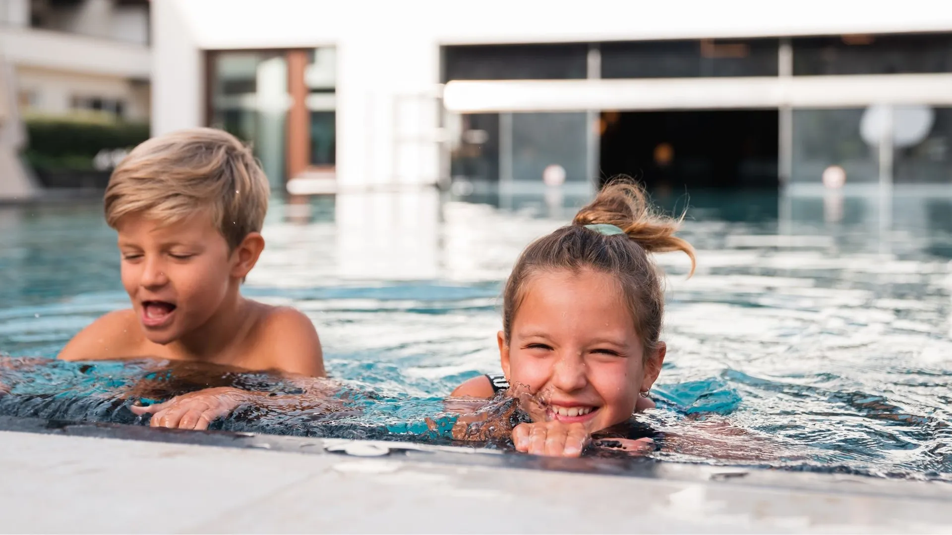 Zwei Kinder lachen im Pool am Beckenrand