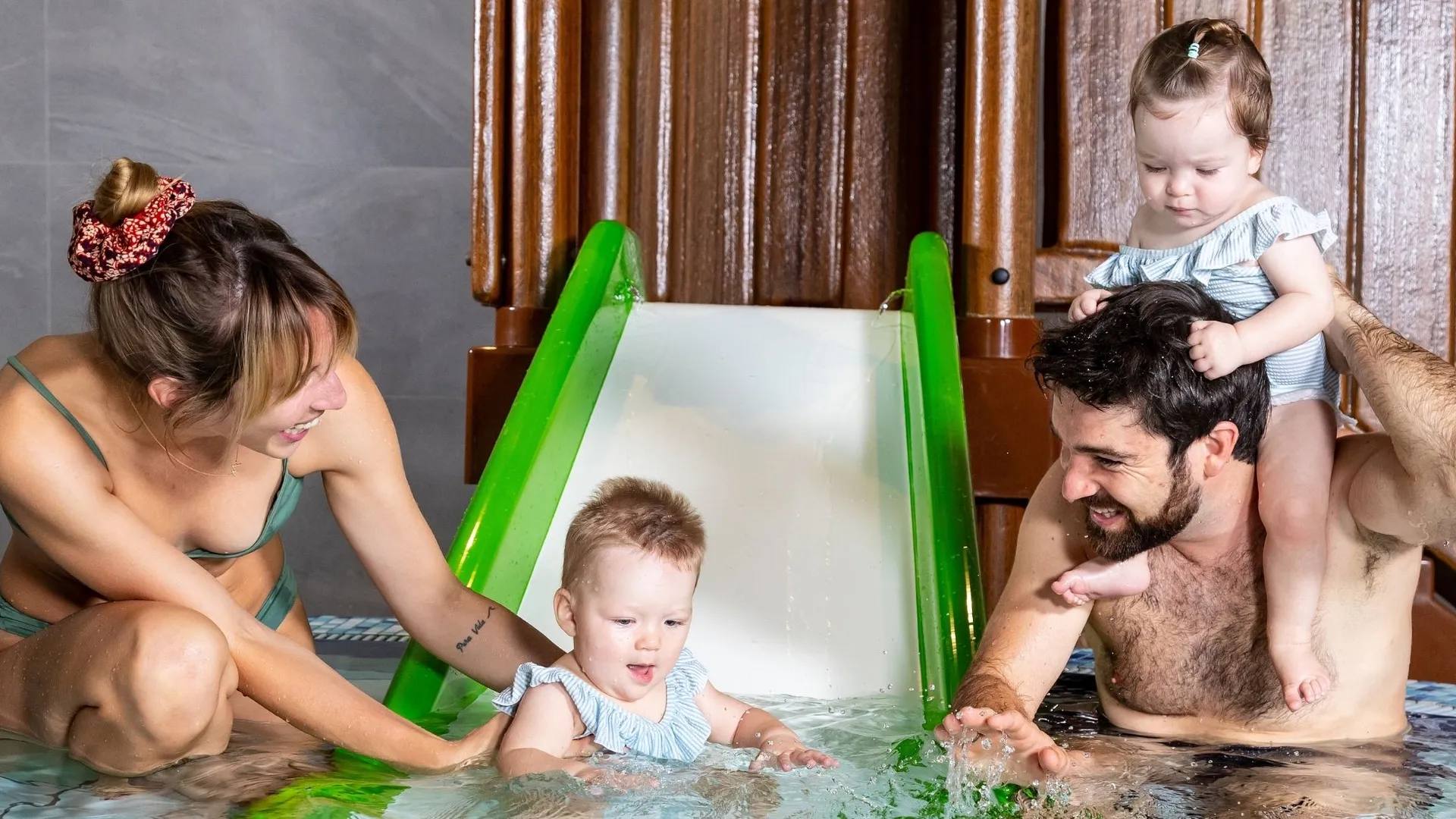 Familie mit Kleinkindern spielt an Wasserrutsche im Kinderbecken