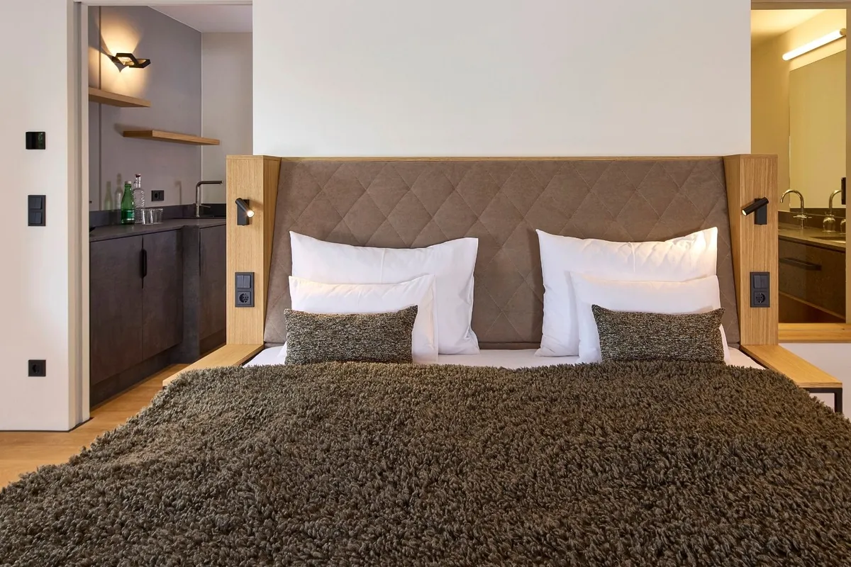 Doppelbett mit gepolstertem Kopfteil, Kitchenette und Bad in einer Hotelsuite