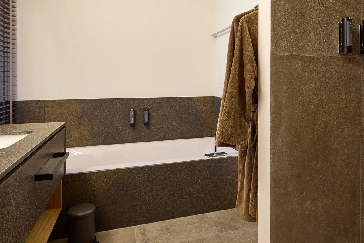 Badezimmer mit Badewanne, Waschtisch und Dusche in Steinoptik