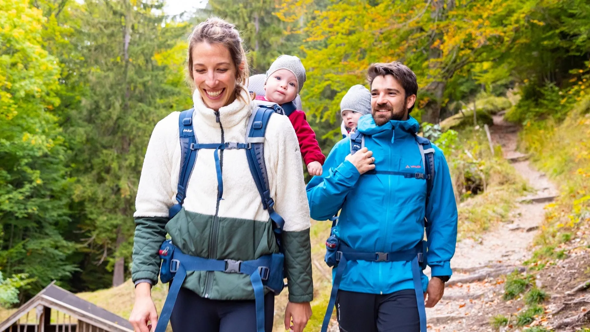 Eltern tragen Kleinkinder in Rückentragen beim Wandern im Wald