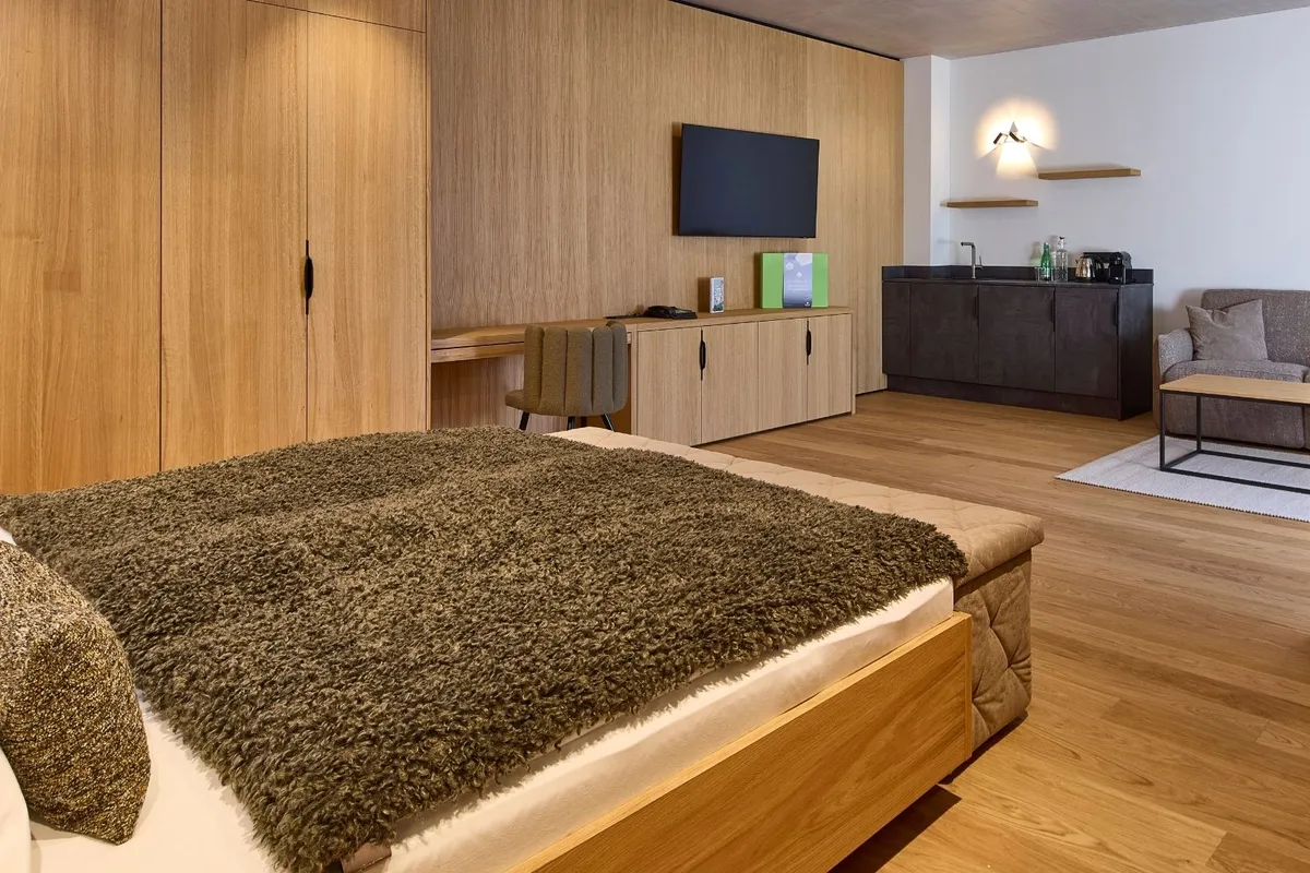 Hotelsuite mit Holzmöbeln, Doppelbett und Sitzecke mit Küchenzeile