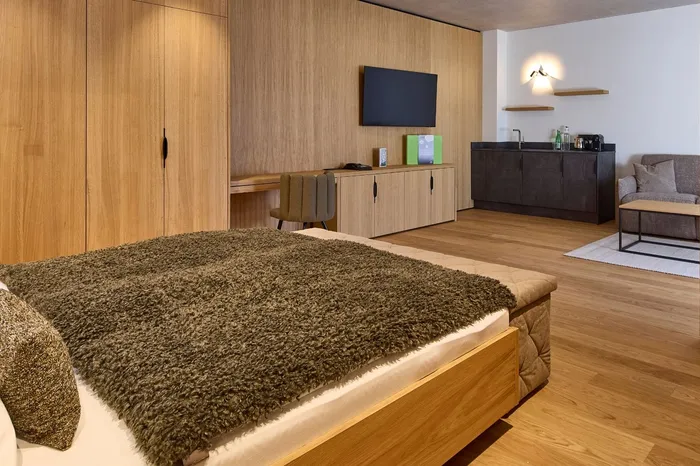 Hotelsuite mit Holzmöbeln, Doppelbett und Sitzecke mit Küchenzeile