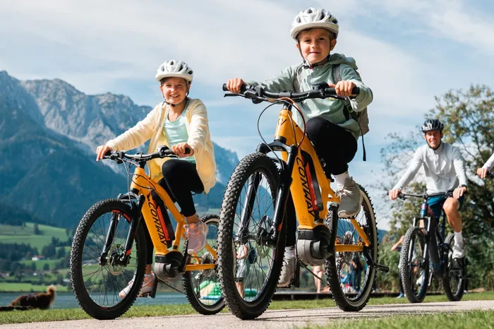 Familie mit Kindern fährt Fahrrad vor Bergkulisse am Walchsee