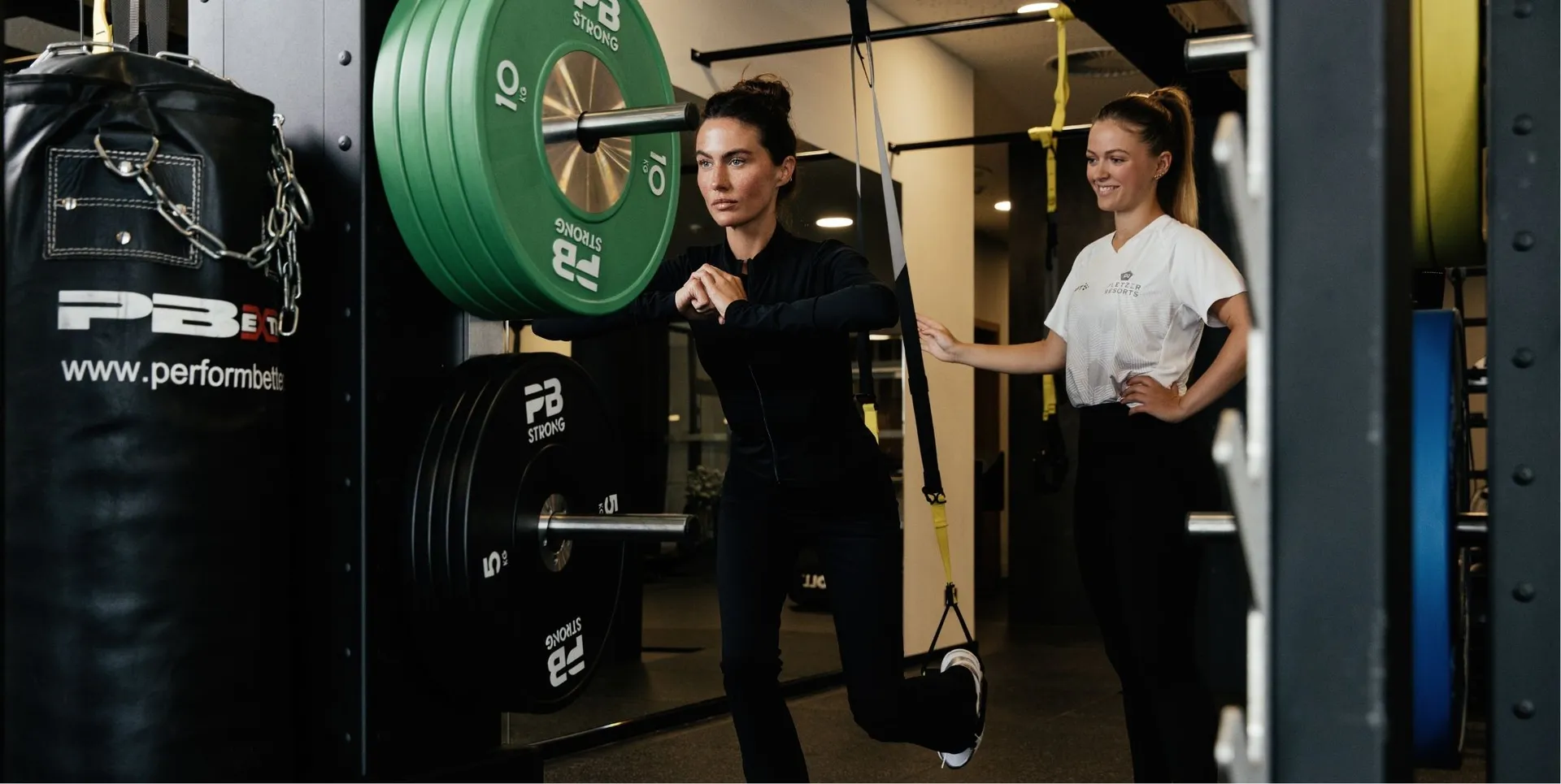 Frau trainiert mit Trainerin an Sling-Trainer im Fitnessstudio