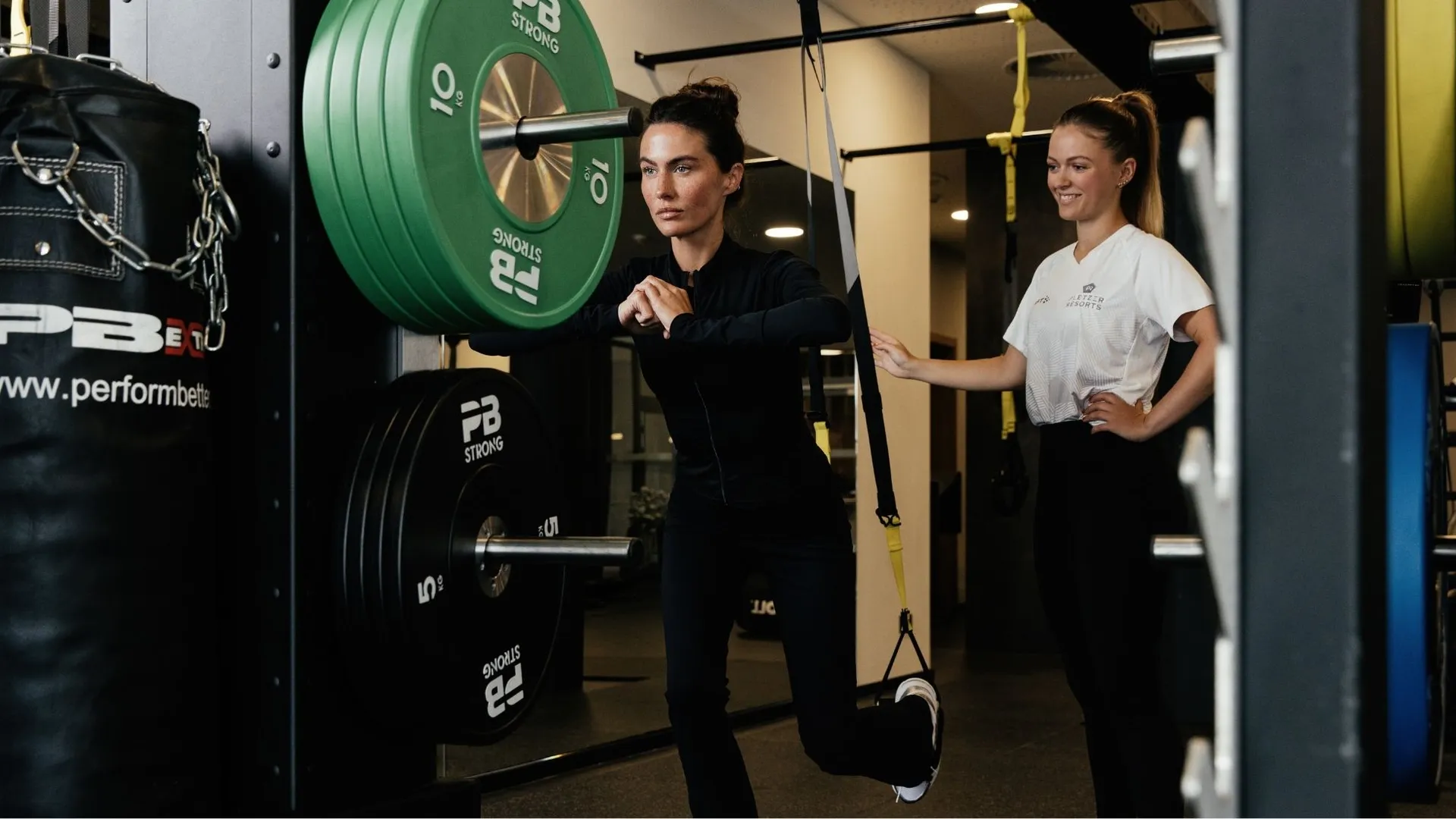 Frau trainiert mit Trainerin an Sling-Trainer im Fitnessstudio