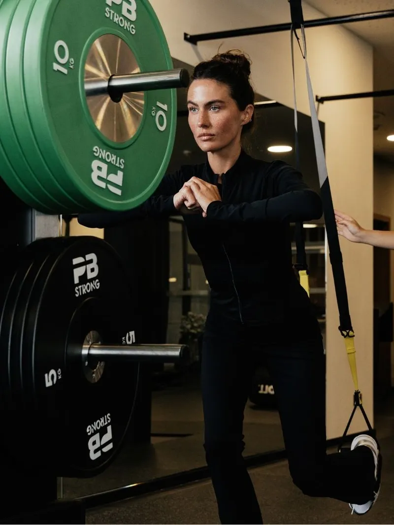 Frau trainiert mit Trainerin an Sling-Trainer im Fitnessstudio