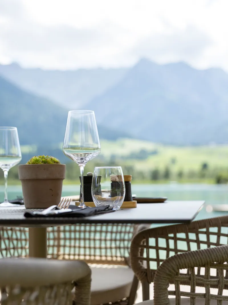 Gedeckter Tisch mit Weingläsern auf Terrasse mit Seeblick und Bergpanorama