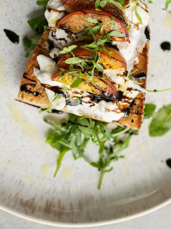 Geröstetes Brot mit Burrata, gegrillten Pfirsichen, Rucola und Balsamico