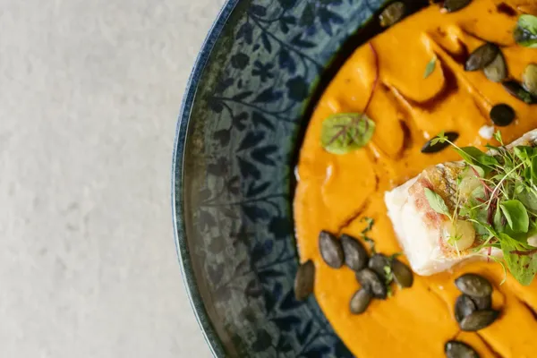 Kürbissuppe mit Fischfilet, Kürbiskernen und Kresse in gemusterter Schale