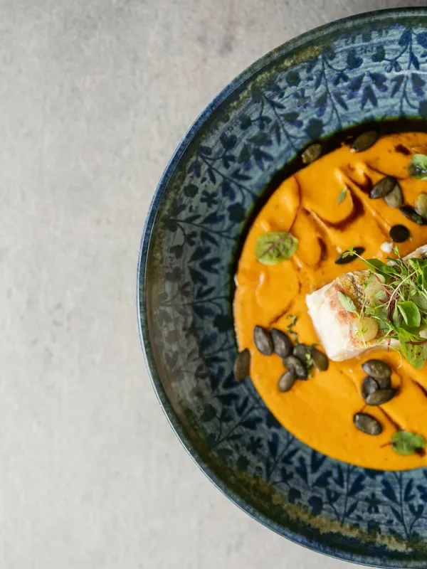 Kürbissuppe mit Fischfilet, Kürbiskernen und Kresse in gemusterter Schale