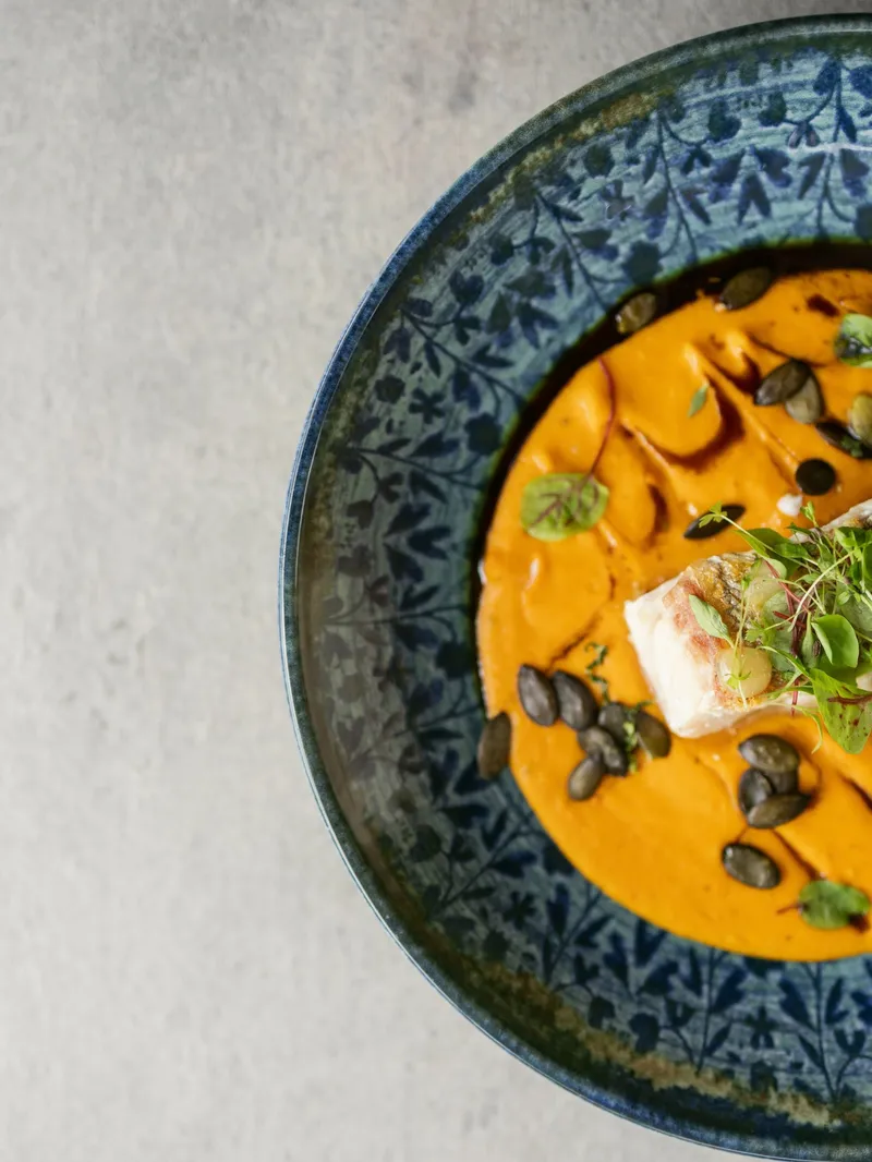 Kürbissuppe mit Fischfilet, Kürbiskernen und Kresse in gemusterter Schale