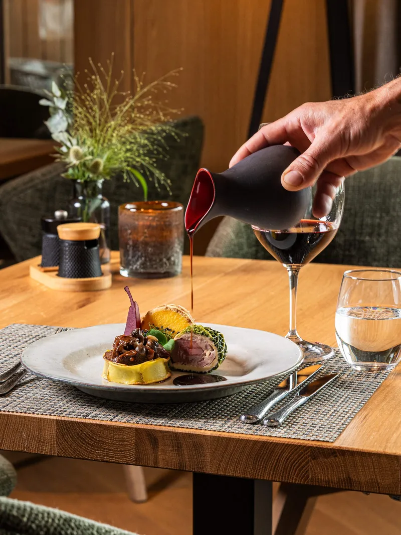 Sauce wird über ein angerichtetes Fleischgericht auf einem Restauranttisch gegossen