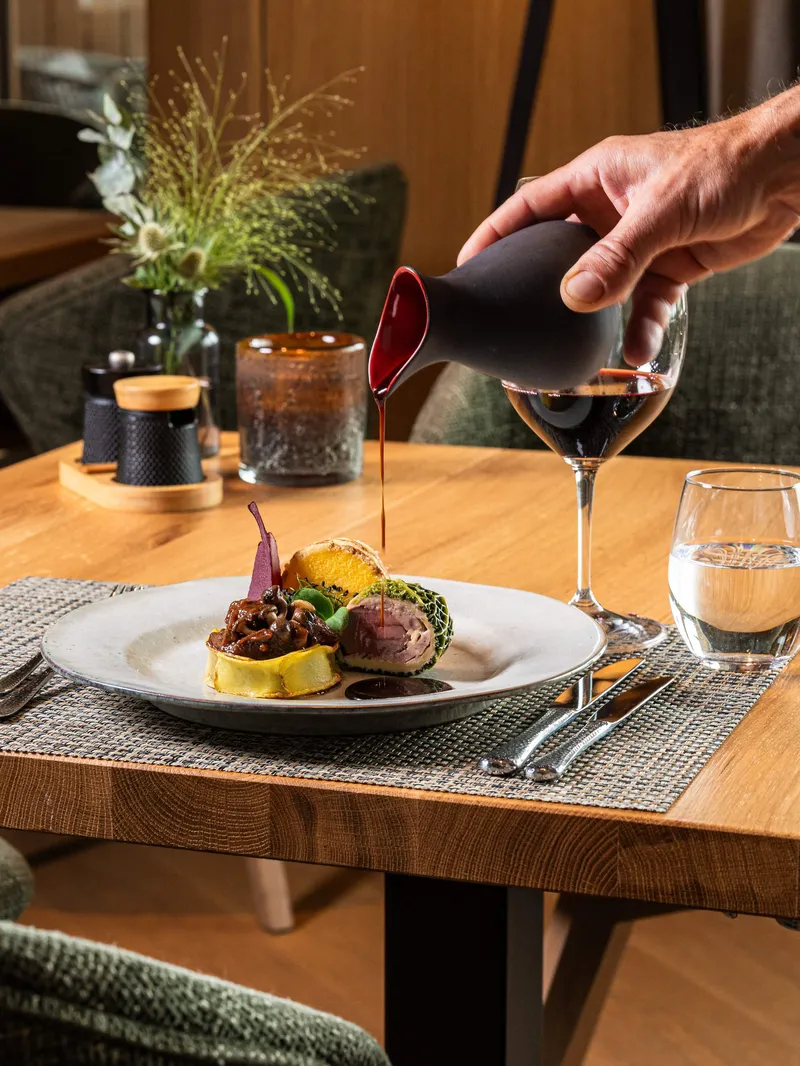 Sauce wird über ein angerichtetes Fleischgericht auf einem Restauranttisch gegossen