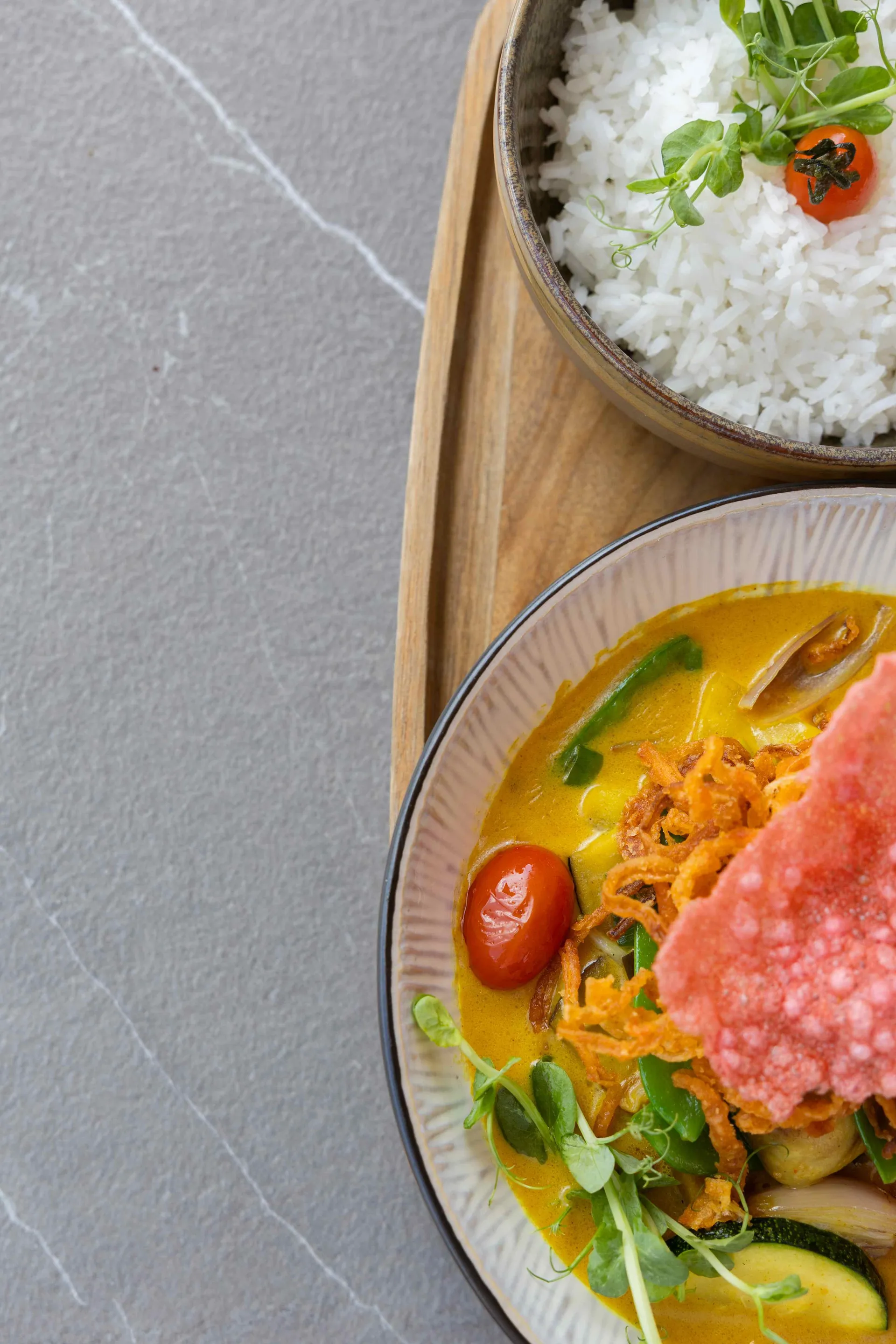 Gelbes Curry mit Gemüse, Cherrytomate und Krupuk neben einer Schale Reis
