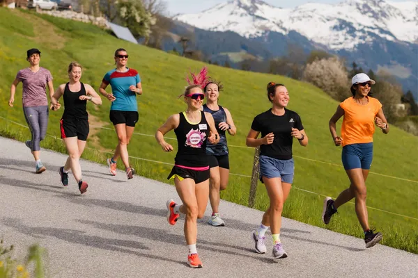 Gruppe von Frauen joggt auf einer Straße vor Bergpanorama