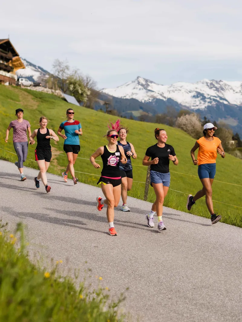 Gruppe von Frauen joggt auf einer Straße vor Bergpanorama
