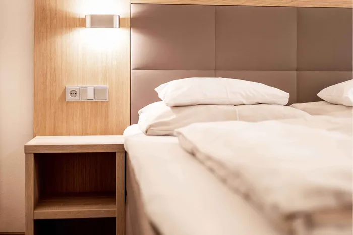 Hotelzimmer mit Bett, Nachttisch und Wandleuchte aus Holz