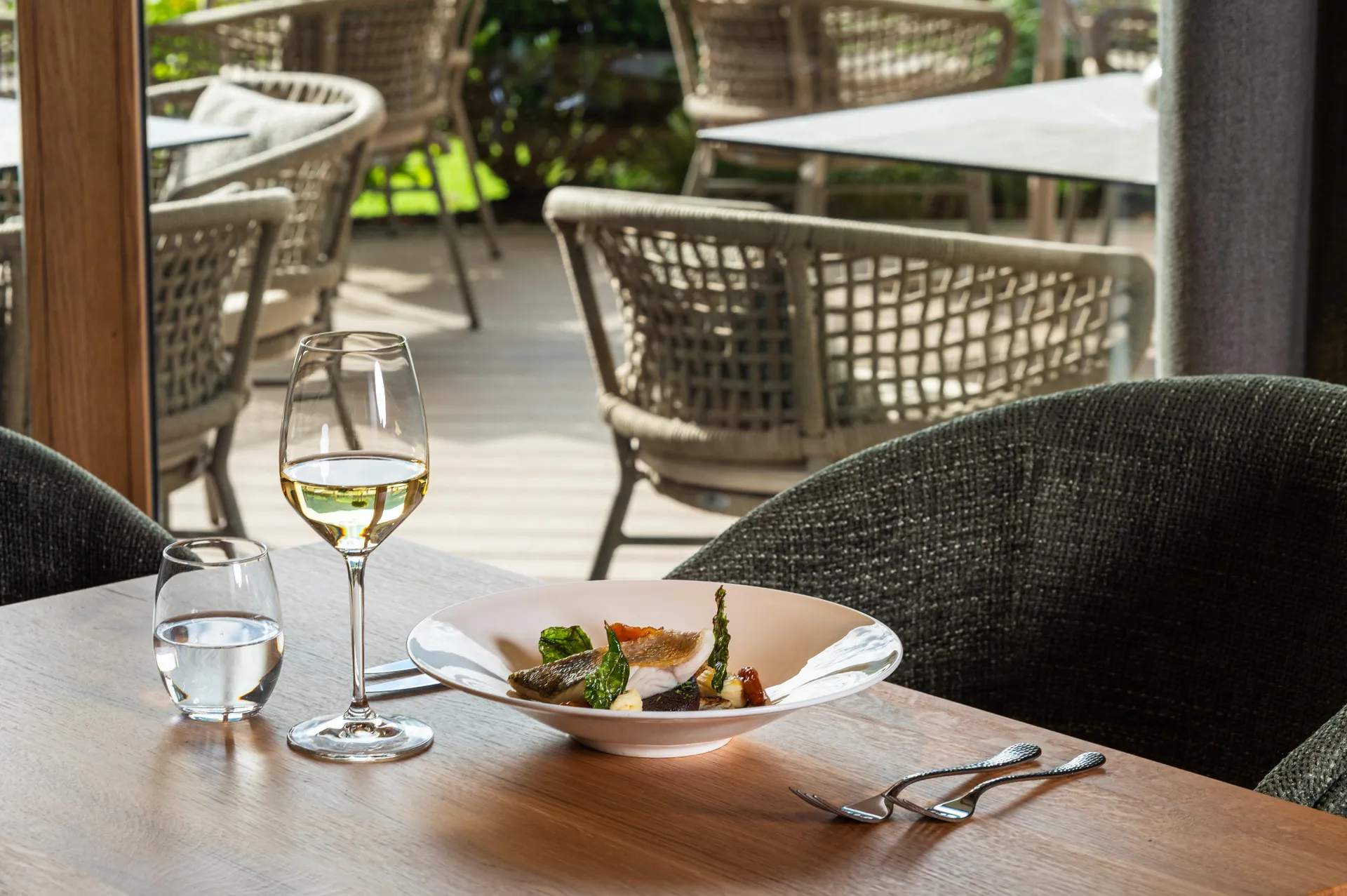 Gedeckter Restauranttisch mit Fischgericht, Weißwein und Blick auf die Terrasse
