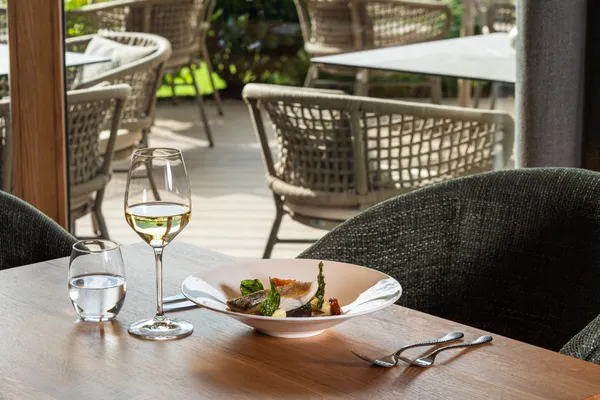 Gedeckter Restauranttisch mit Fischgericht, Weißwein und Blick auf die Terrasse
