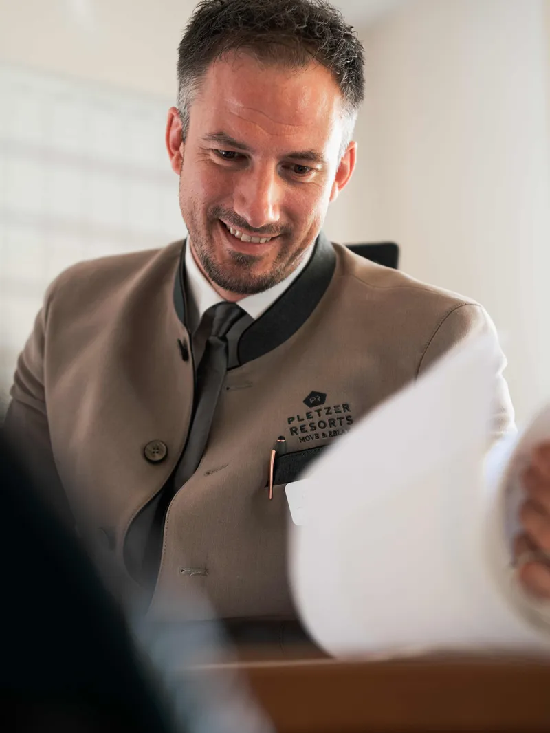 Lächelnder Mitarbeiter in Pletzer-Resorts-Uniform an der Rezeption