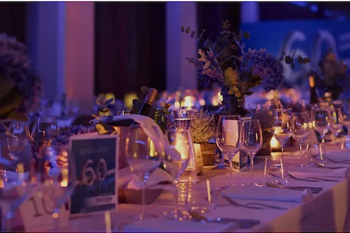 Festlich gedeckte lange Tafel mit Gläsern, Blumen, Kerzen und der Zahl 60, beleuchtet in Blau und Lila.