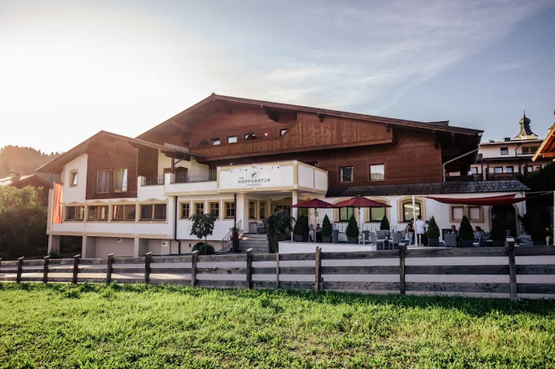 Alpenhotel Hopfgarten mit Terrasse, Sonnenschirmen und umliegender Wiese