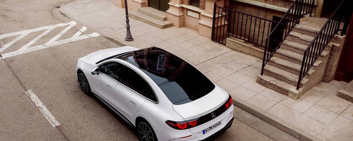 Vue aérienne d'une Mercedes-Benz blanche avec toit panoramique sombre, garée près d'un escalier en pierre.