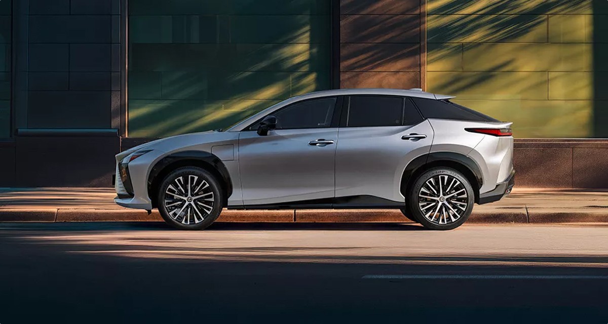 SUV électrique Lexus RZ gris argenté vu de profil, garé devant un bâtiment moderne aux reflets dorés.