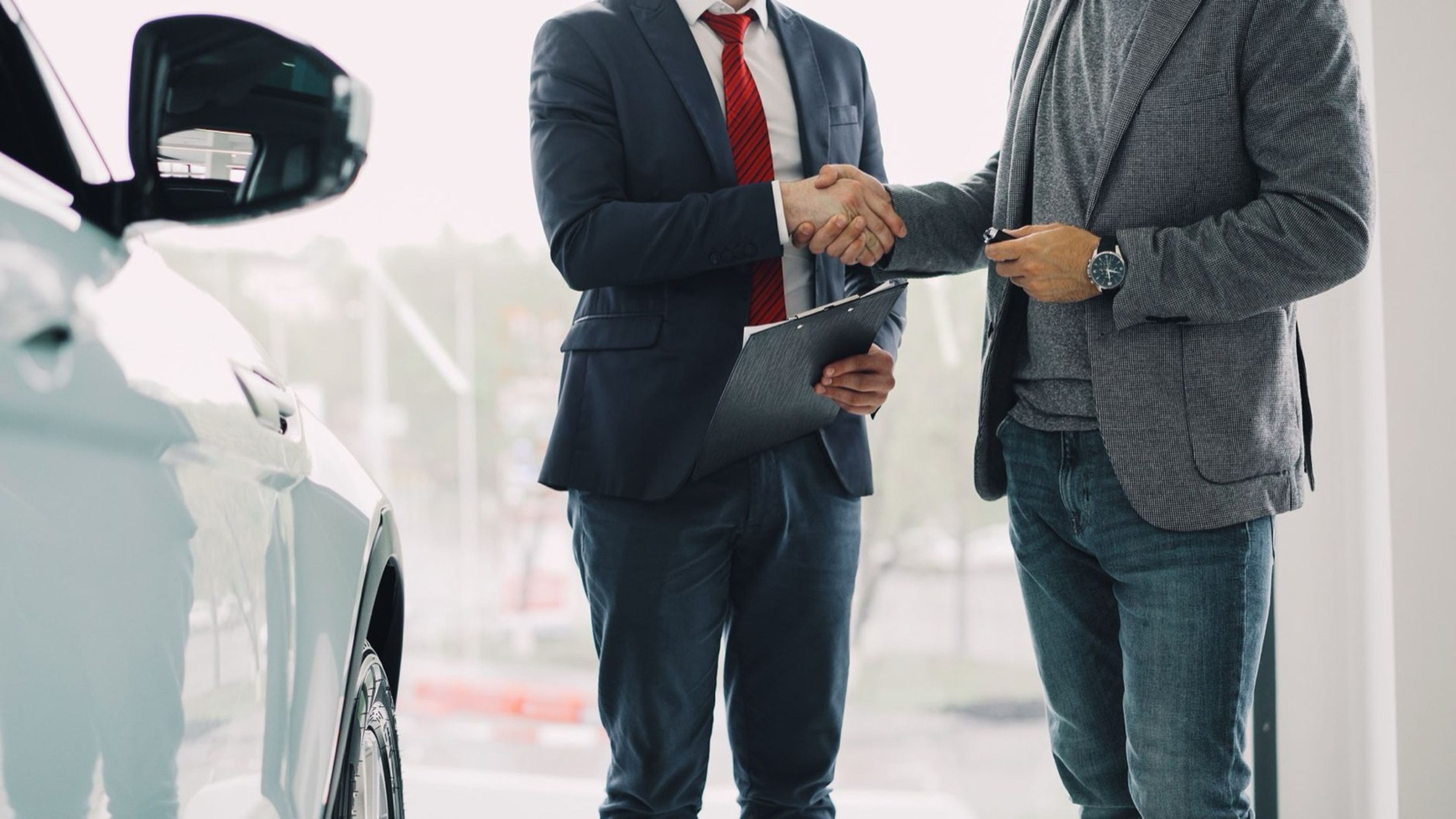 Deux hommes se serrant la main dans une concession automobile, symbolisant la réussite d'une transaction commerciale
