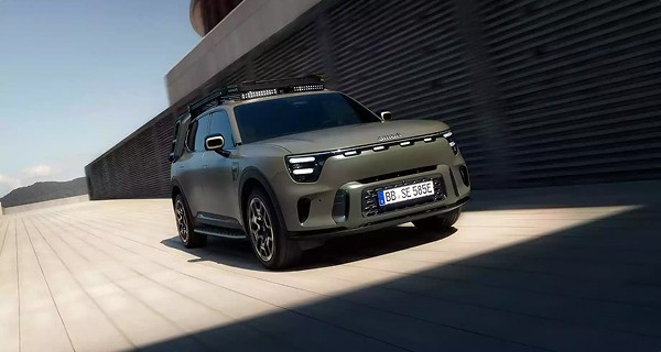 SUV électrique kaki avec galerie de toit, phares LED et plaque bleue européenne, roulant sur une surface moderne.