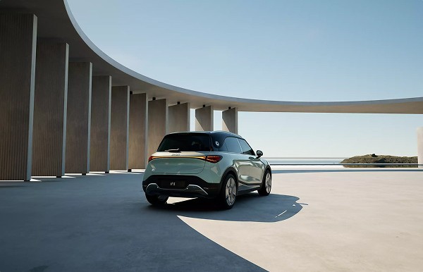 Vue arrière d'un SUV électrique vert menthe garé devant une architecture moderne arrondie, avec mer et ciel bleu en fond.