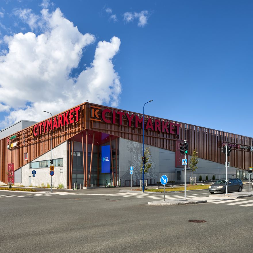 Modern shopping center with "Citymarket" signage, located at a street intersection under a clear blue sky with some clouds.