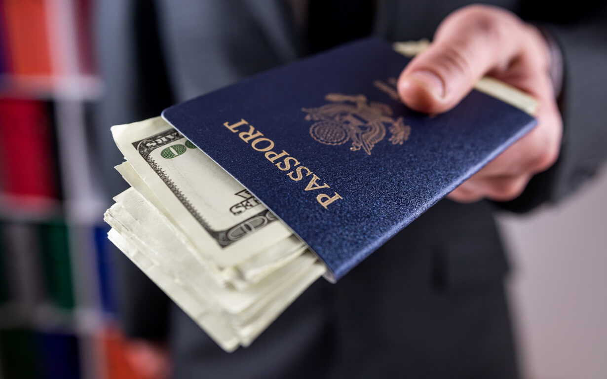 A person in a suit holds out a passport with U.S. dollar bills peeking out, subtly highlighting international money transfer limits in the US. The focus is on the passport and money, with a blurred background.