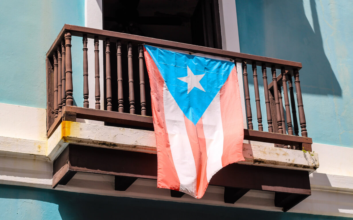 A Puerto Rican flag graces a rustic wooden balcony against a turquoise wall.