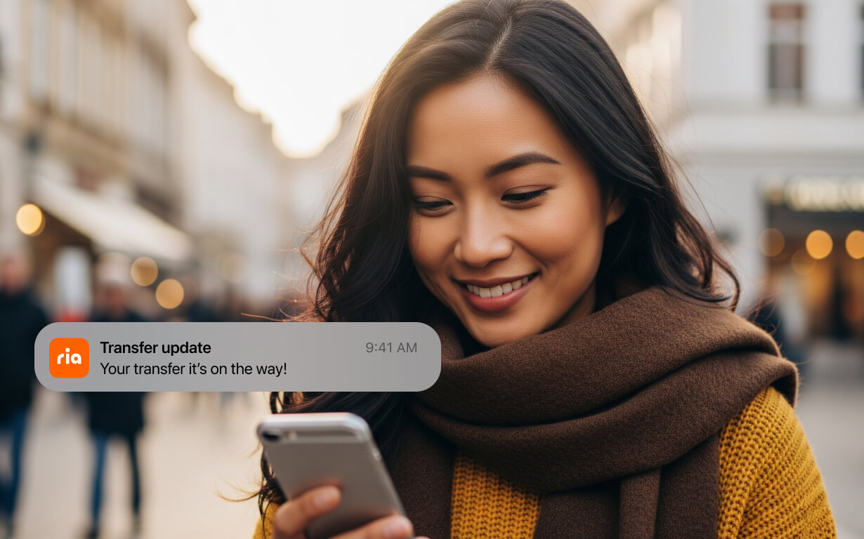 A woman with long dark hair and a brown scarf smiles while looking at her phone outdoors. A notification on her phone says, “Money transfer canceled: Please try again. 9:41 AM.”.