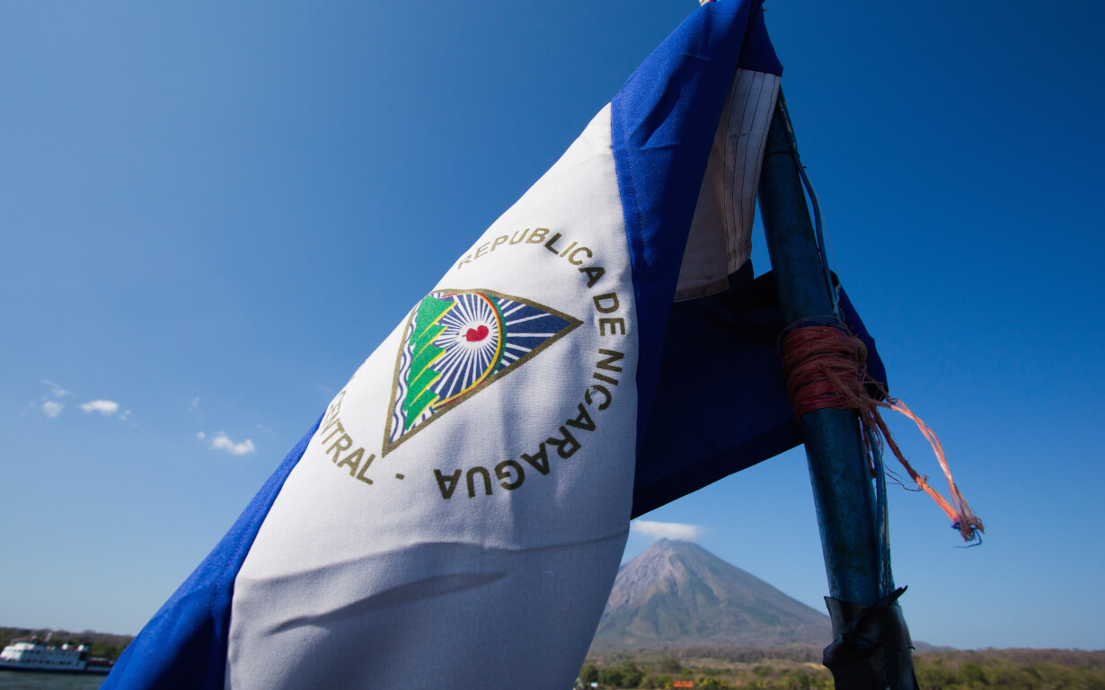 The image shows the flag of Nicaragua attached to a pole, with the flag's emblem and the words "Republica de Nicaragua, America Central" are visible.