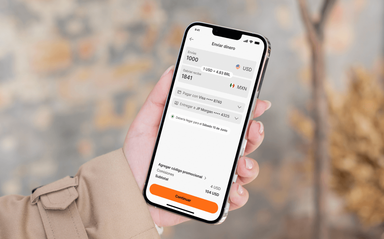 A person holds a smartphone displaying a money transfer app in Spanish, showing how to send money from the US—sending 1000 USD and delivering 1841 MXN to Mexico—with payment options and a highlighted “Continuar” button.