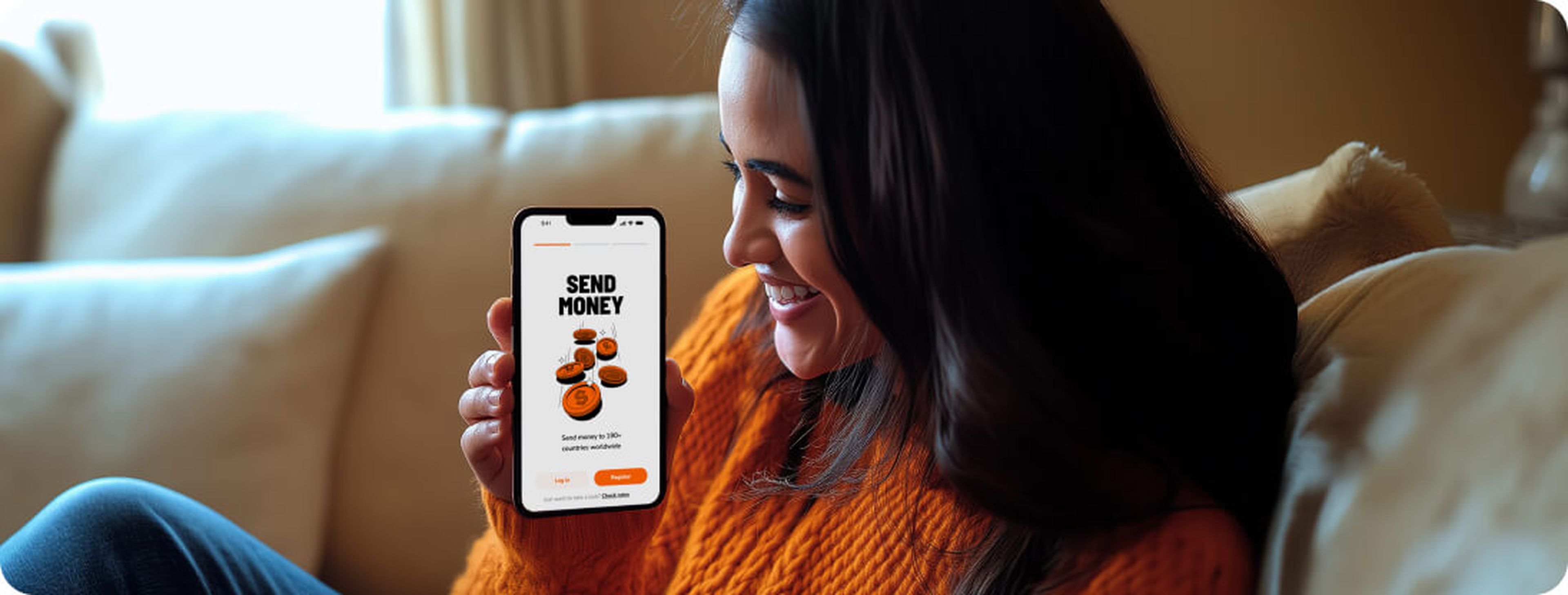 A woman in an orange sweater smiles while looking at a smartphone screen displaying a financial app with the text "Send Money" and images of coins. She's effortlessly managing her currency transfer, sitting comfortably on a beige couch.