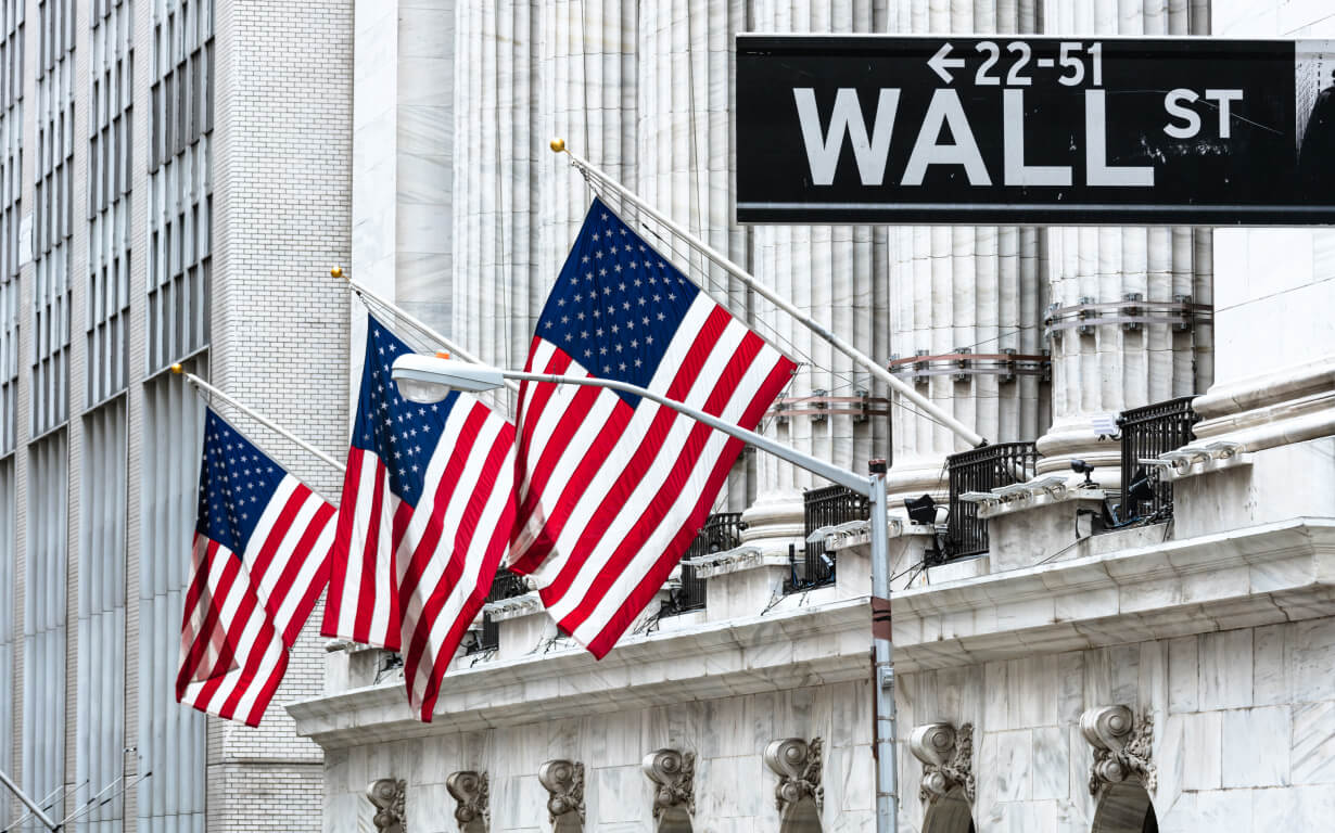 Three American flags wave in front of a large white building with stone columns. A street sign above reads "Wall St" with directional arrows. The cityscape, evoking a sense of business district ambiance, hints at the bustling world of currency transfer and classic architectural details.
