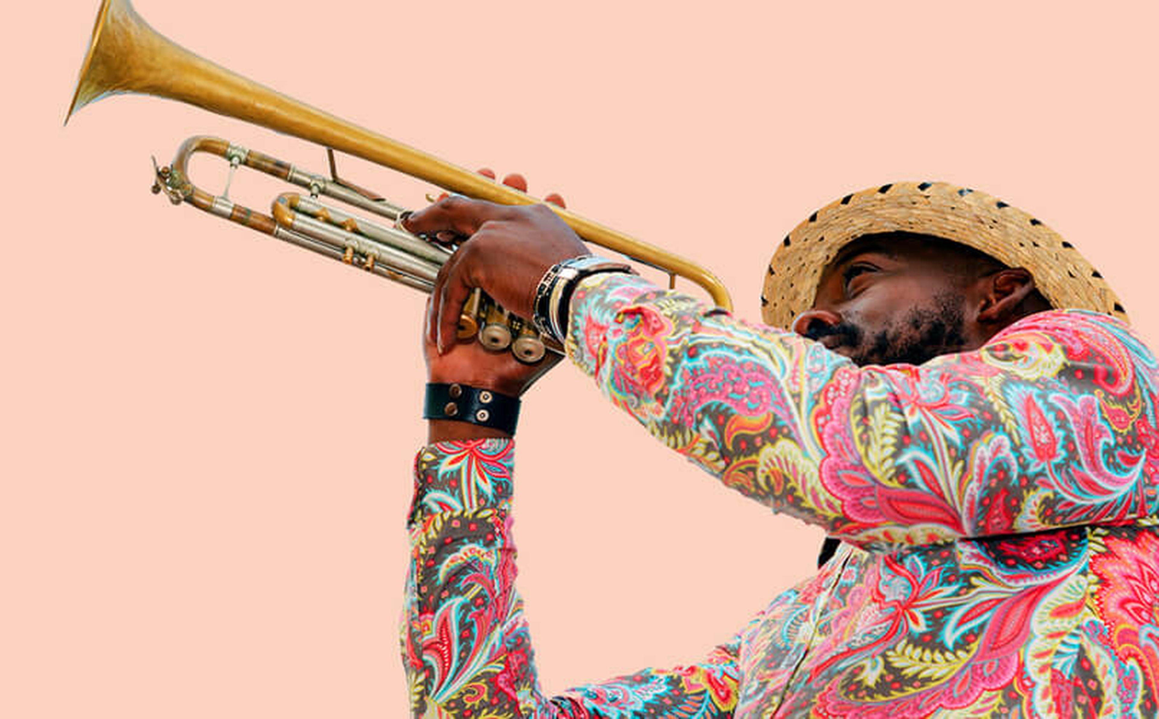 A musician wearing a straw hat and a colorful, patterned shirt plays a trumpet against a solid peach-colored background. The angle captures the musician's side profile, highlighting the intricate design of their shirt and the brass of the trumpet, reminiscent of festivals in Latin America.