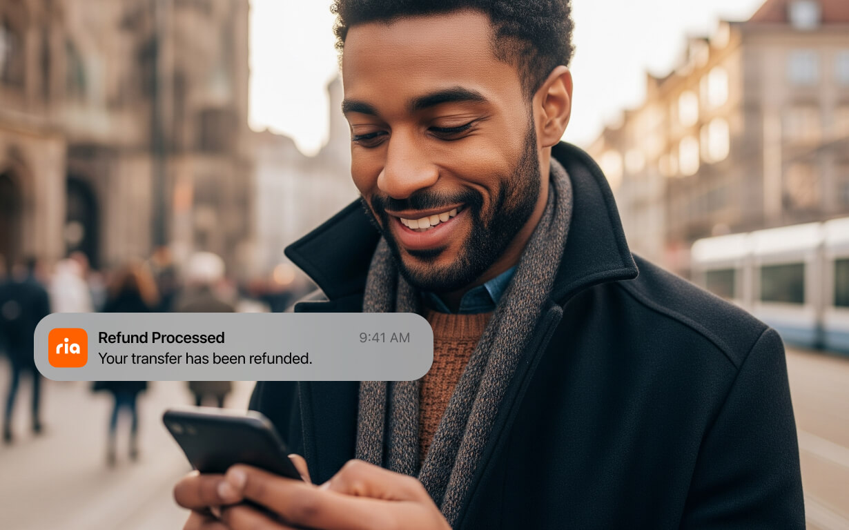 A man smiles while looking at his phone outdoors. On the screen, a notification reads, "Money transfer canceled. Refund Processed. Your transfer has been refunded.