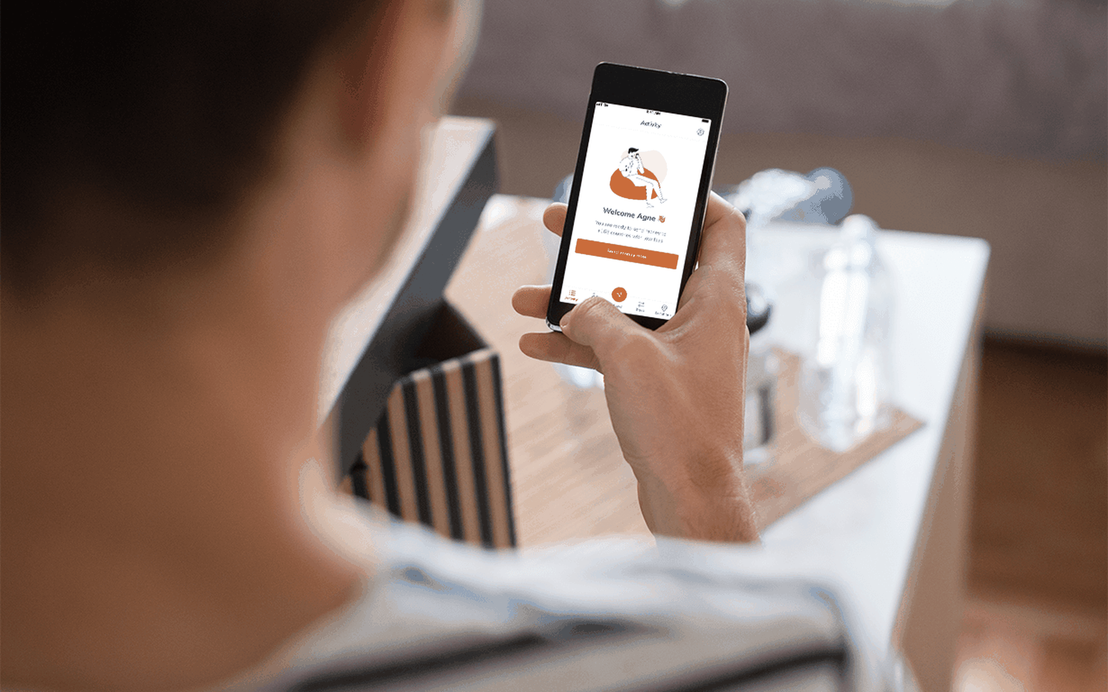 A person is holding a smartphone displaying a health and wellness app with a jogging theme. The background features a table with a water bottle and wooden box, creating an atmosphere akin to addressing taxes while tackling international money transfers in your workout or home setting.
