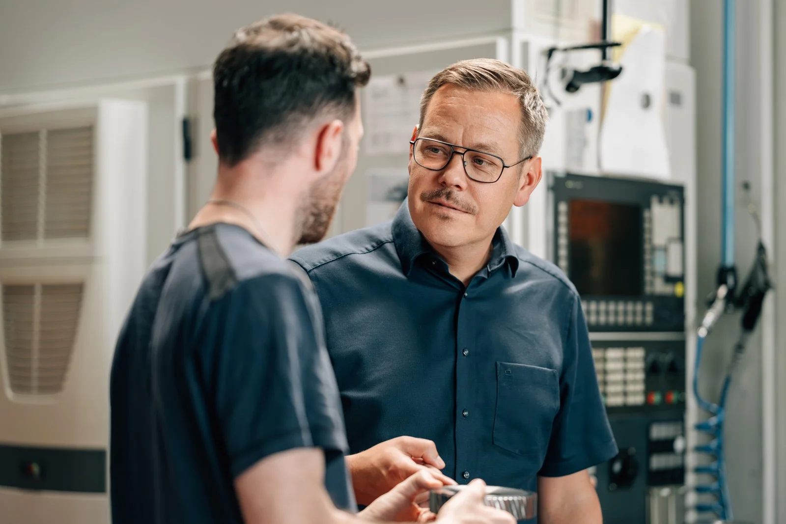 Zwei Mitarbeitende im Gespräch über ein Werkstück an der Maschine