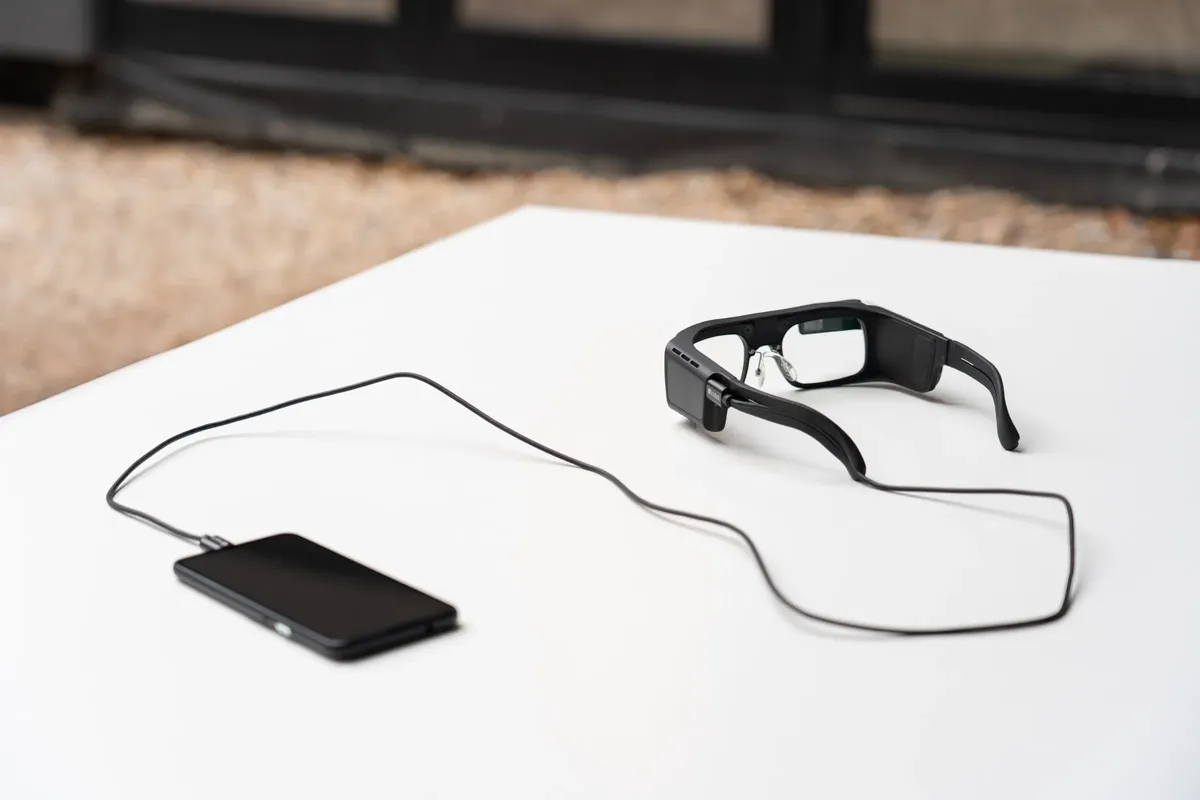 The Iristick.G3 on a white table, connected to a smartphone by its USB-C cable.