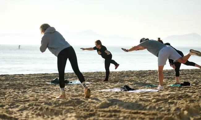 Gruppe von Menschen trainiert am Sandstrand Gleichgewicht bei Meer- und Bergkulisse.
