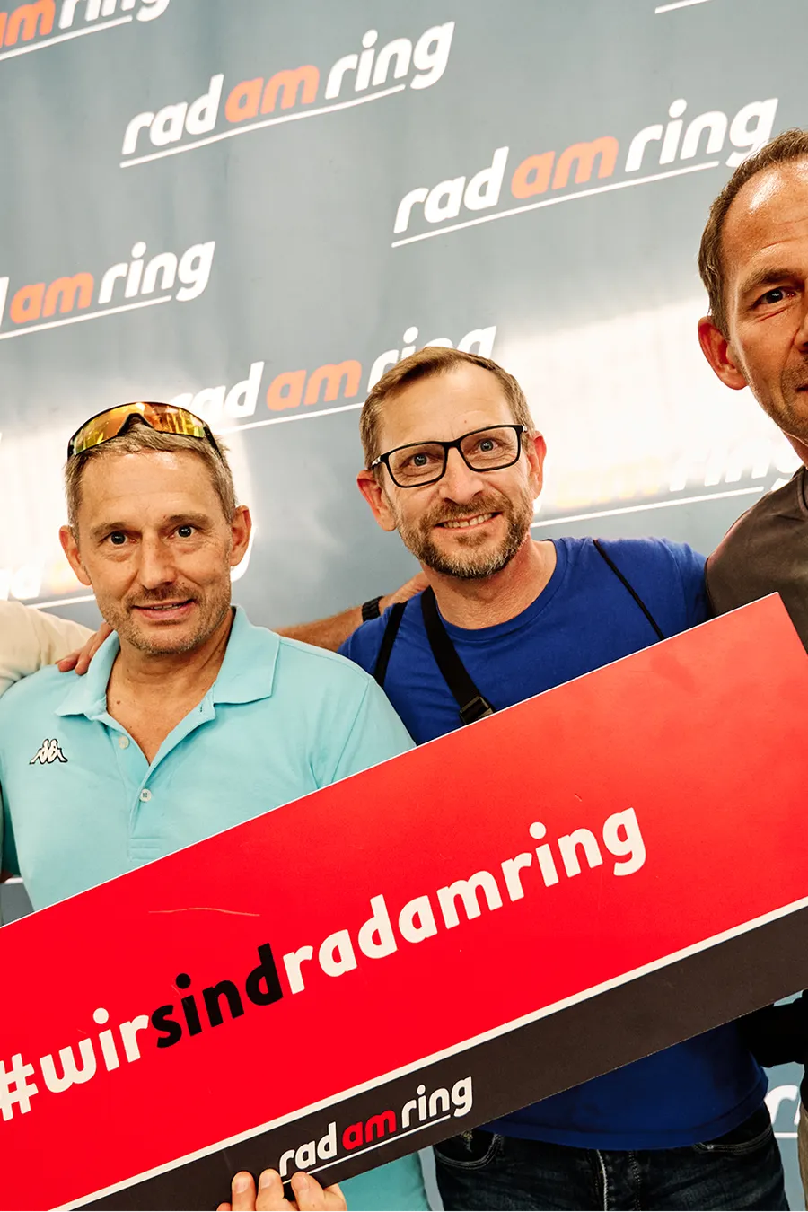 4 Personen an der Rad am Ring Photowall halten ein Schild mit dem Text #wirsindradamring
