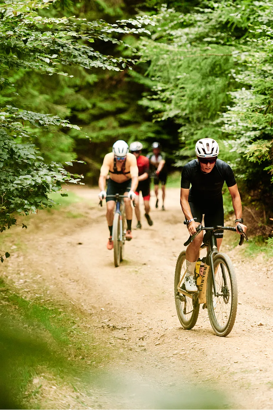 Cyclists riding on a dirt path through a lush, green forest.