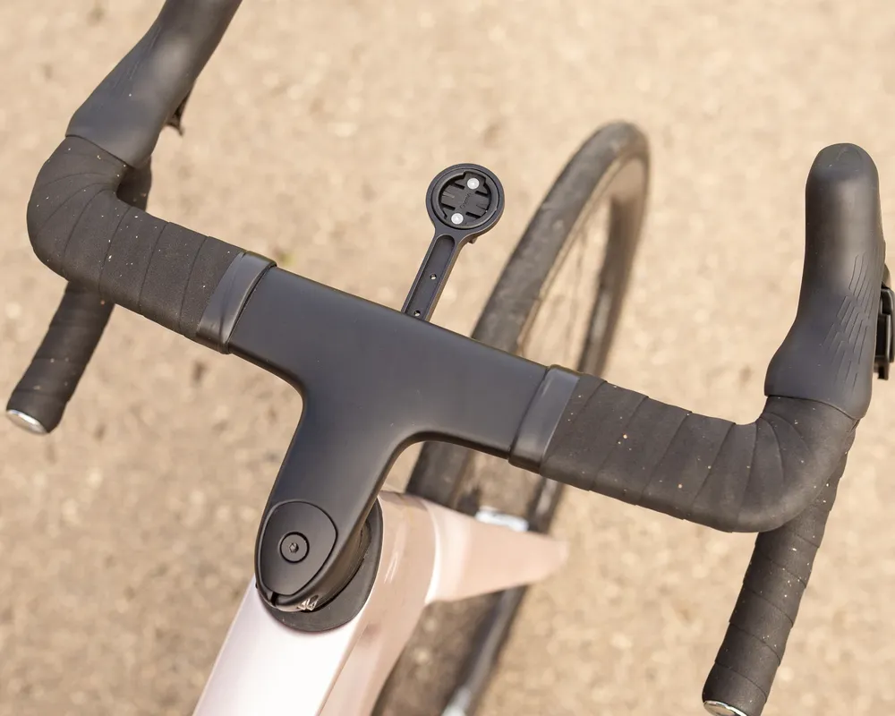 Nahaufnahme des integrierten Lenkers eines Rennrads in hellem Rosé. Schwarzes Lenkerband und eine Garmin Computerhalterung sind zu sehen.