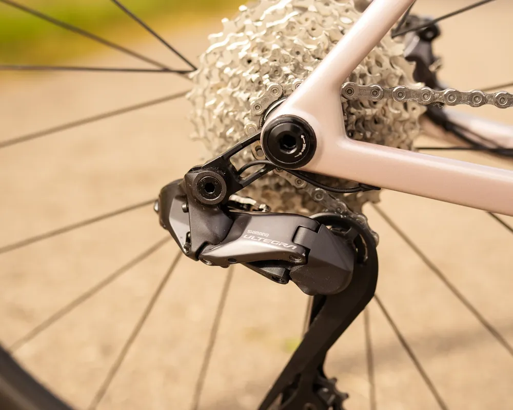 Nahaufnahme eines Shimano Ultegra Schaltwerks an einem beigen Fahrradrahmen mit silberner Kassette und Kette am Hinterrad.